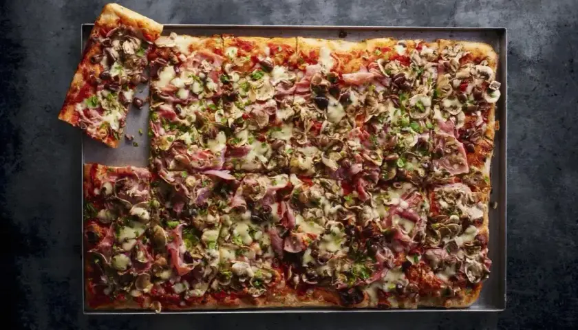 Domowa pizza na blachę z szynką, pieczarkami i oliwkami. Idealny przepis na szybki obiad.