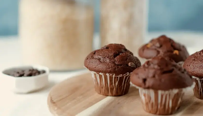 Pyszne muffinki z czekoladą, gotowe do zjedzenia. W tle słoiki z cukrem i mąką.