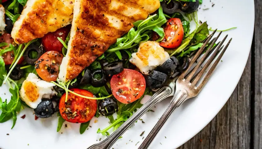 Pyszna sałatka z grillowanym halloumi, pomidorkami koktajlowymi i czarnymi oliwkami na talerzu, gotowa do zjedzenia.