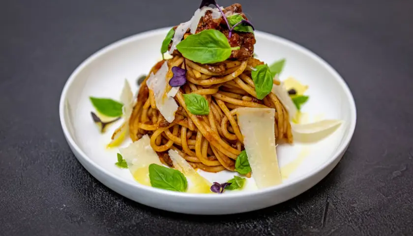 Pyszne spaghetti alla norma z sosem pomidorowym, bakłażanem i parmezanem, ozdobione listkami bazylii.