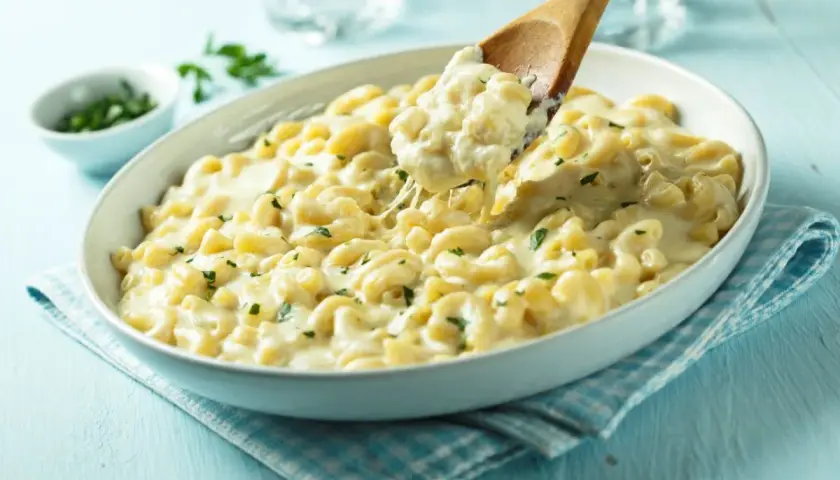 Pyszne mac and cheese przepis w białej misce, z drewnianą łyżką nabierającą porcję kremowego makaronu z serem.