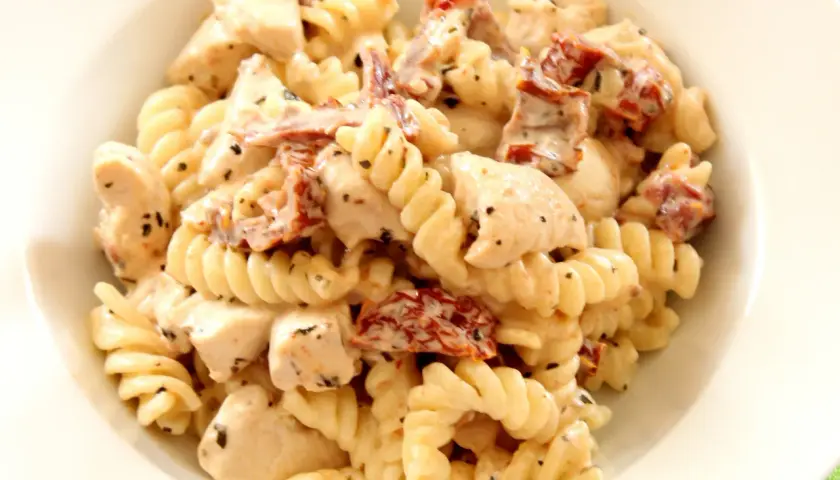 Pyszny makaron fusilli z kawałkami kurczaka i aromatycznymi suszonymi pomidorami w kremowym sosie.