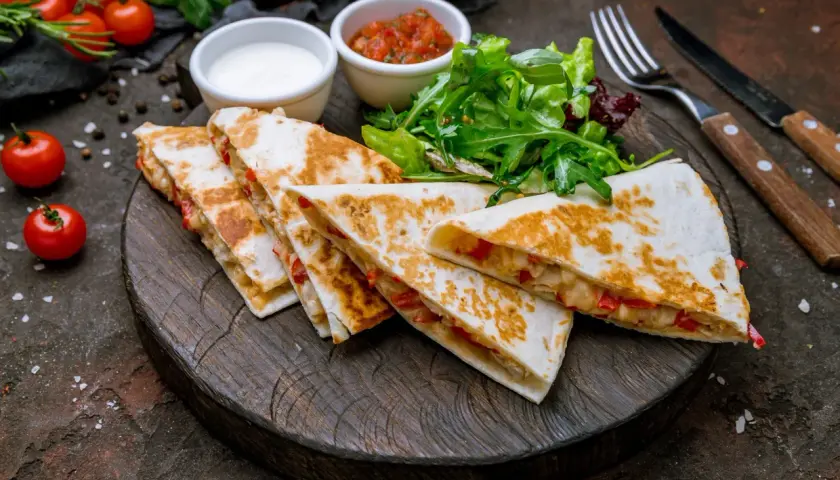 Pyszna quesadilla z kurczakiem, podana z salsą, śmietaną i sałatką na drewnianej desce.