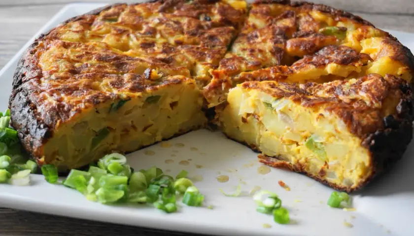 Pyszna tortilla de patatas, pokrojona na kawałki, z zieloną cebulką na talerzu.