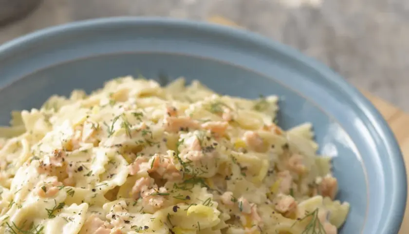 Pyszny makaron farfalle z kawałkami łososia w kremowym sosie, posypany świeżym koperkiem i pieprzem.