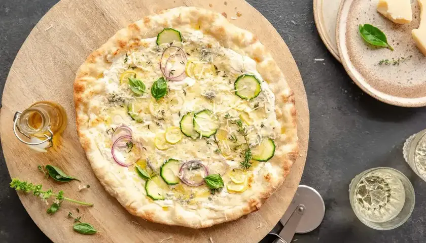 Pyszny spód do pizzy z cukinią, cebulą i ziołami, podany na drewnianej desce.