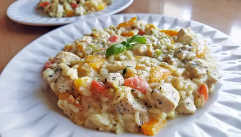 Pyszne risotto z kurczakiem, papryką i bazylią, podane na białym talerzu. Idealne na obiad.