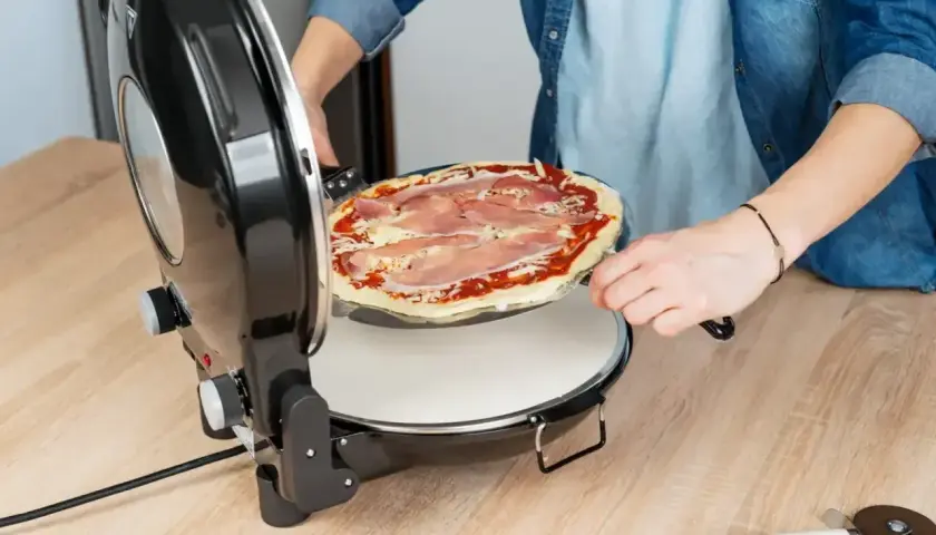 Osoba wkłada pizzę z szynką do pieca. Szybko i łatwo przygotujesz idealną pizzę w domu.