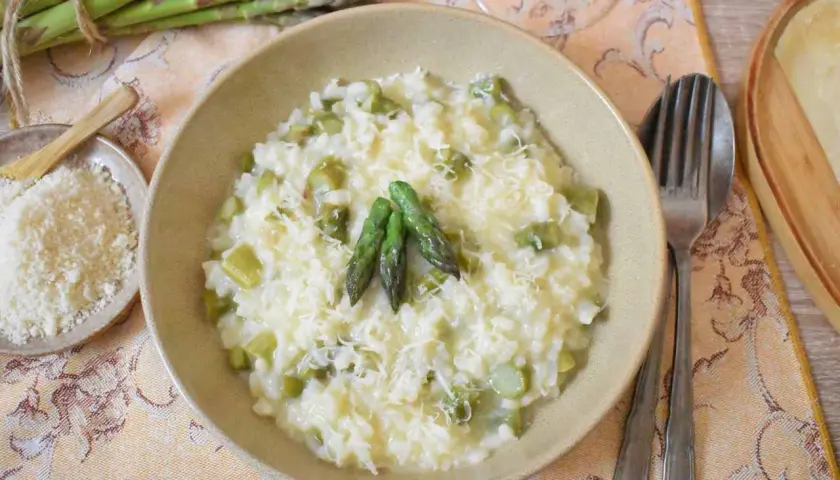 Kremowe risotto ze szparagami, posypane parmezanem, z trzema młodymi pędami szparagów na wierzchu.