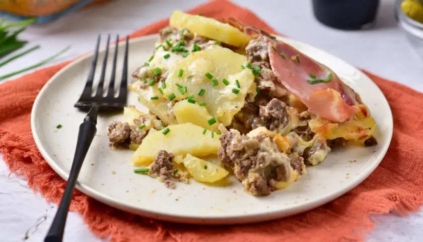 Zapiekanka ziemniaczana z mięsem mielonym, jak u Ani Gotuje, na talerzu, posypana szczypiorkiem. Pyszne danie!