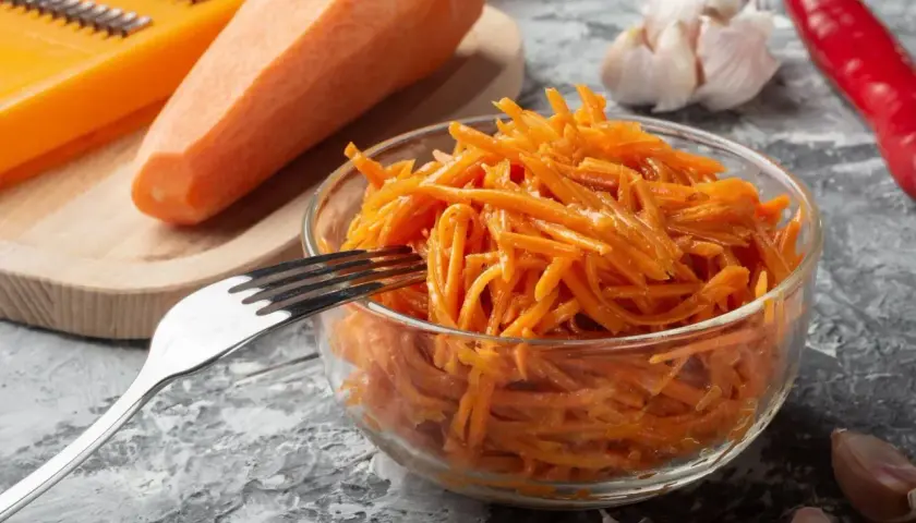 Pyszna surówka z marchewki, gotowa do podania. Obok świeża marchewka, tarka, czosnek i papryczka chili.