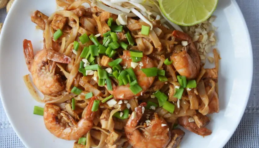 Pyszne pad thai z krewetkami, makaronem ryżowym, tofu i szczypiorkiem, podane z limonką i orzeszkami ziemnymi.