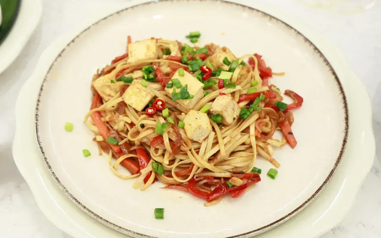 Pyszny makaron z tofu, papryką i szczypiorkiem, posypany chili. Danie wygląda apetycznie i kolorowo.