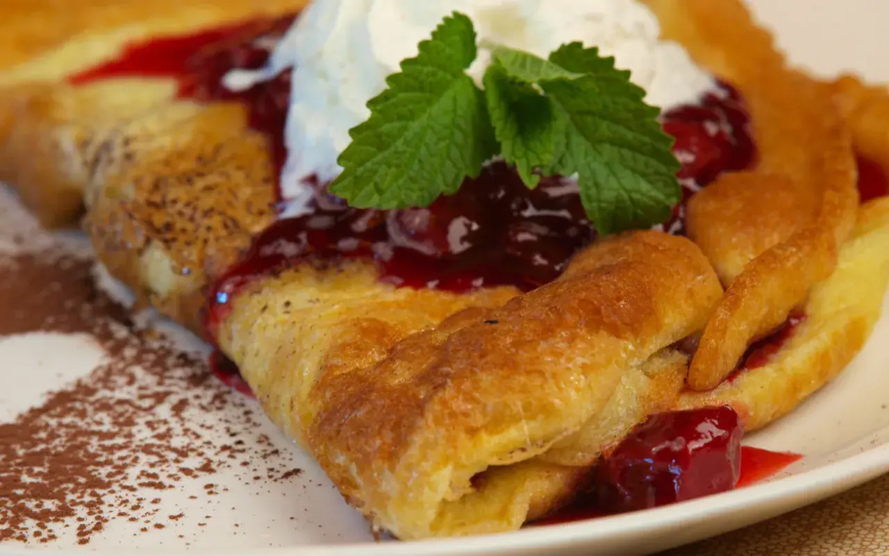 Pyszny omlet Ani gotuje się z wiśniami i bitą śmietaną, posypany kakao.