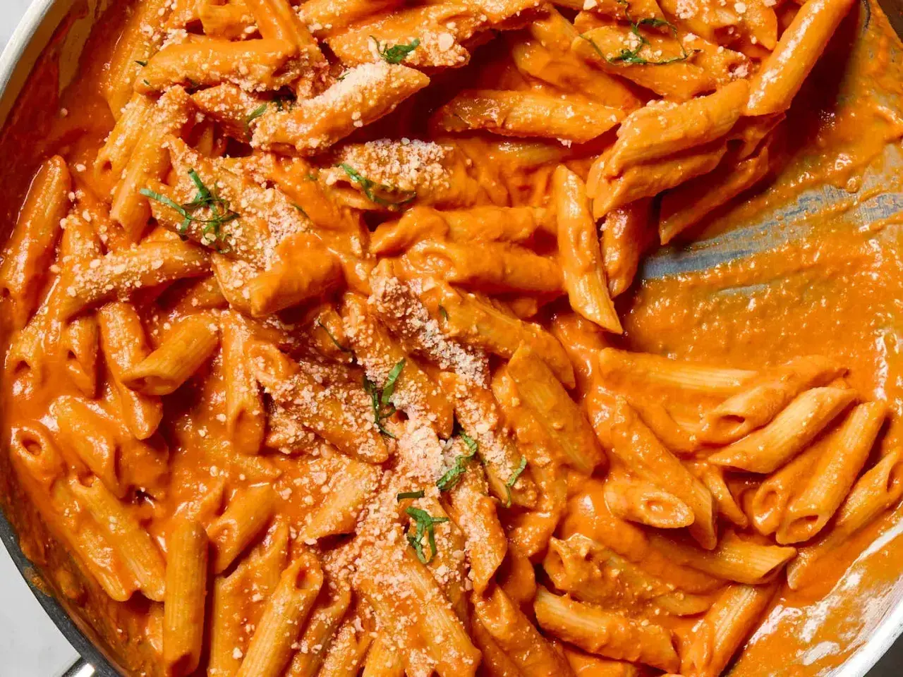 Penne alla vodka w kremowym, pomarańczowym sosie, posypane parmezanem i bazylią.
