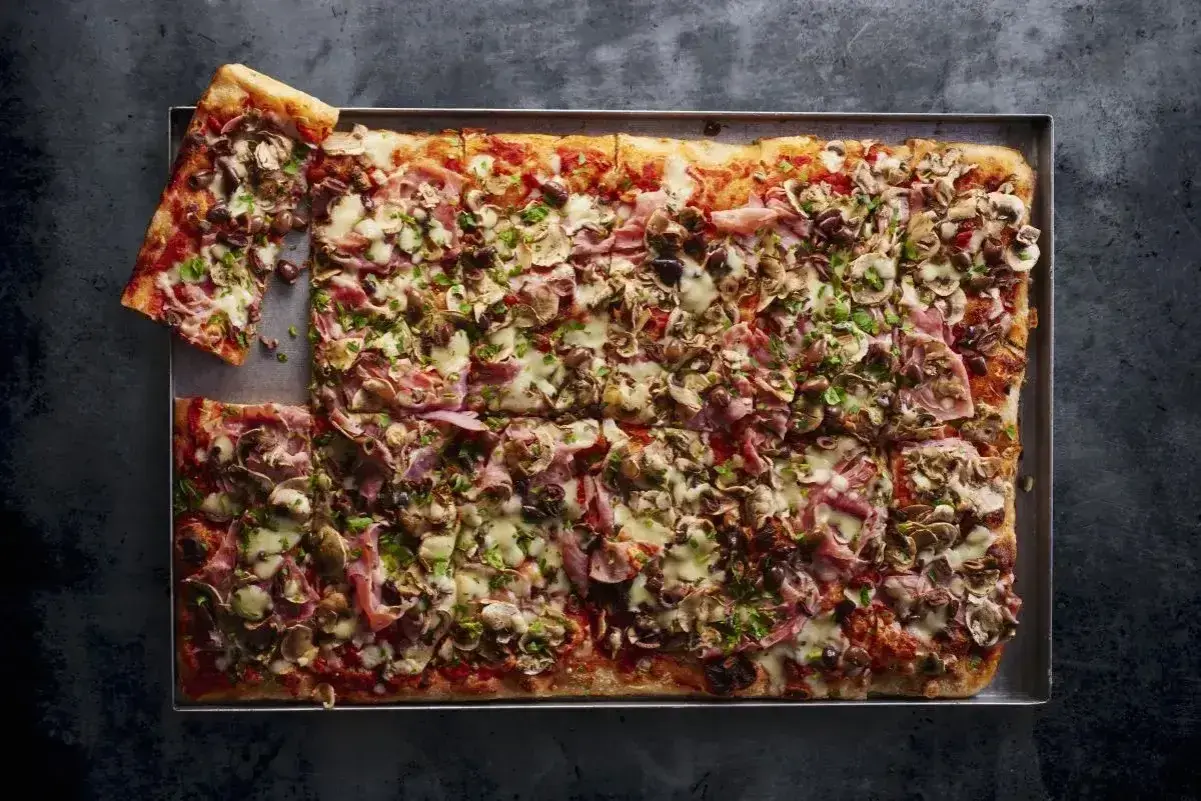 Domowa pizza na blachę z szynką, pieczarkami i oliwkami. Idealny przepis na szybki obiad.