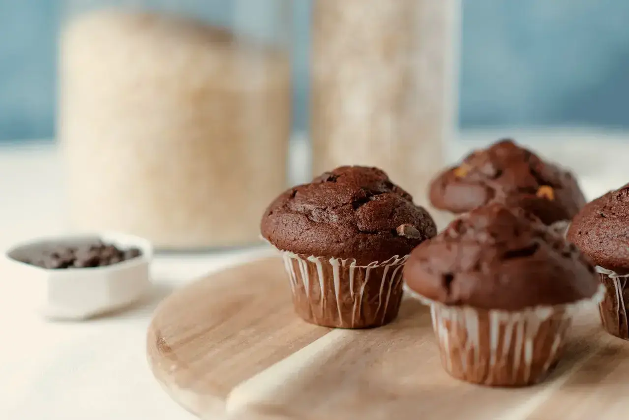 Pyszne muffinki z czekoladą, gotowe do zjedzenia. W tle słoiki z cukrem i mąką.