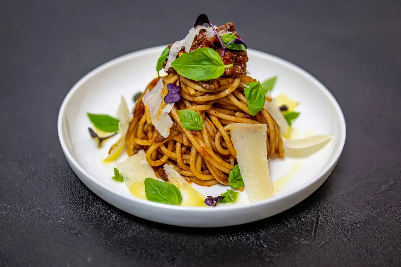 Pyszne spaghetti alla norma z sosem pomidorowym, bakłażanem i parmezanem, ozdobione listkami bazylii.