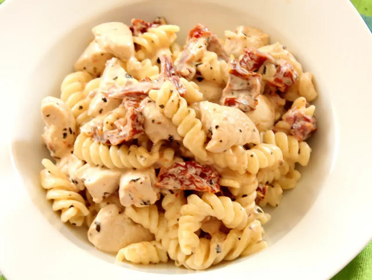 Pyszny makaron fusilli z kawałkami kurczaka i aromatycznymi suszonymi pomidorami w kremowym sosie.