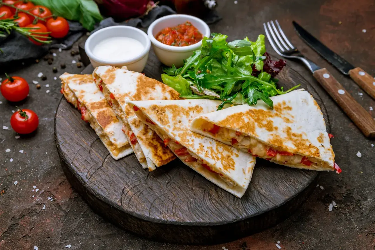 Pyszna quesadilla z kurczakiem, podana z salsą, śmietaną i sałatką na drewnianej desce.
