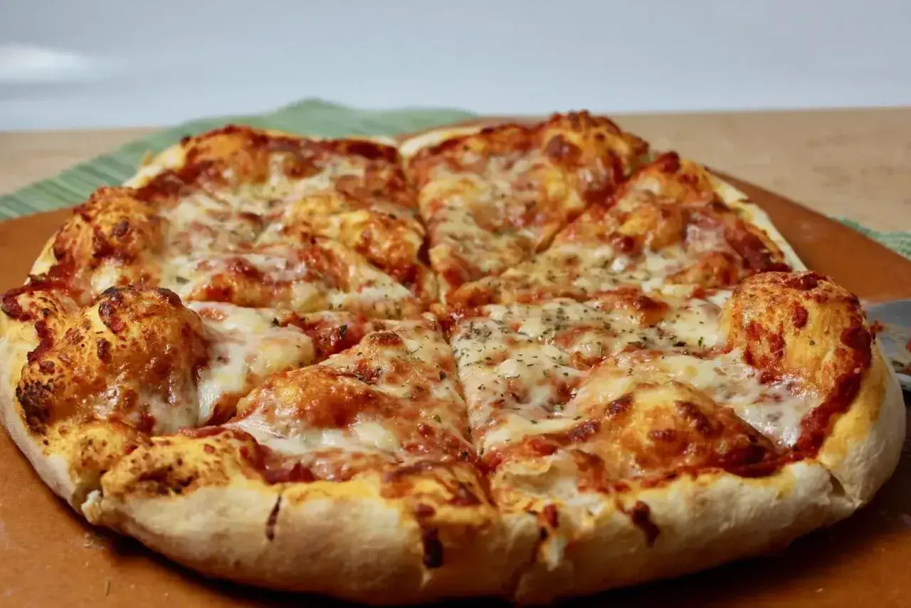 Pyszne, gorące ciasto na pizzę z ciągnącym się serem i aromatycznymi ziołami, pokrojone na kawałki.