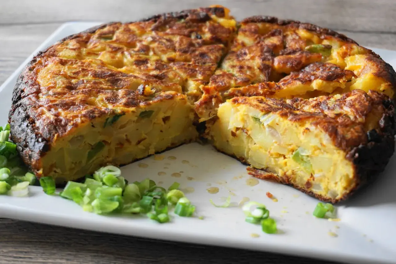 Pyszna tortilla de patatas, pokrojona na kawałki, z zieloną cebulką na talerzu.