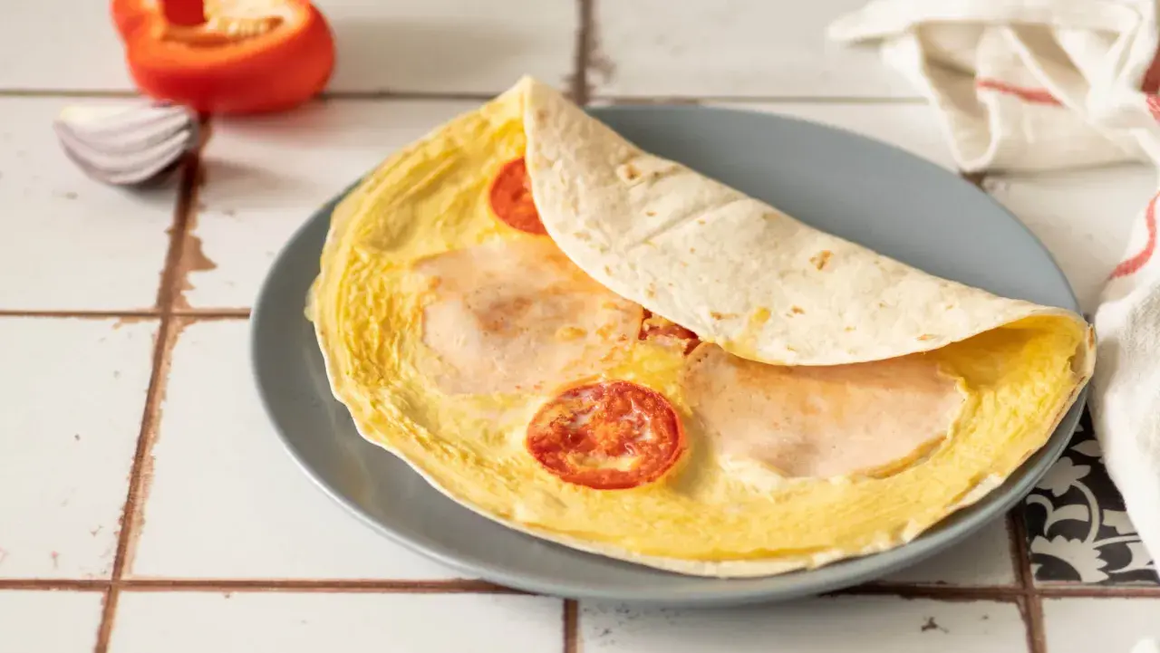 Pyszna, ciepła kolacja: omlet z tortillą, pomidorkami i szynką. Idealny na szybki posiłek.