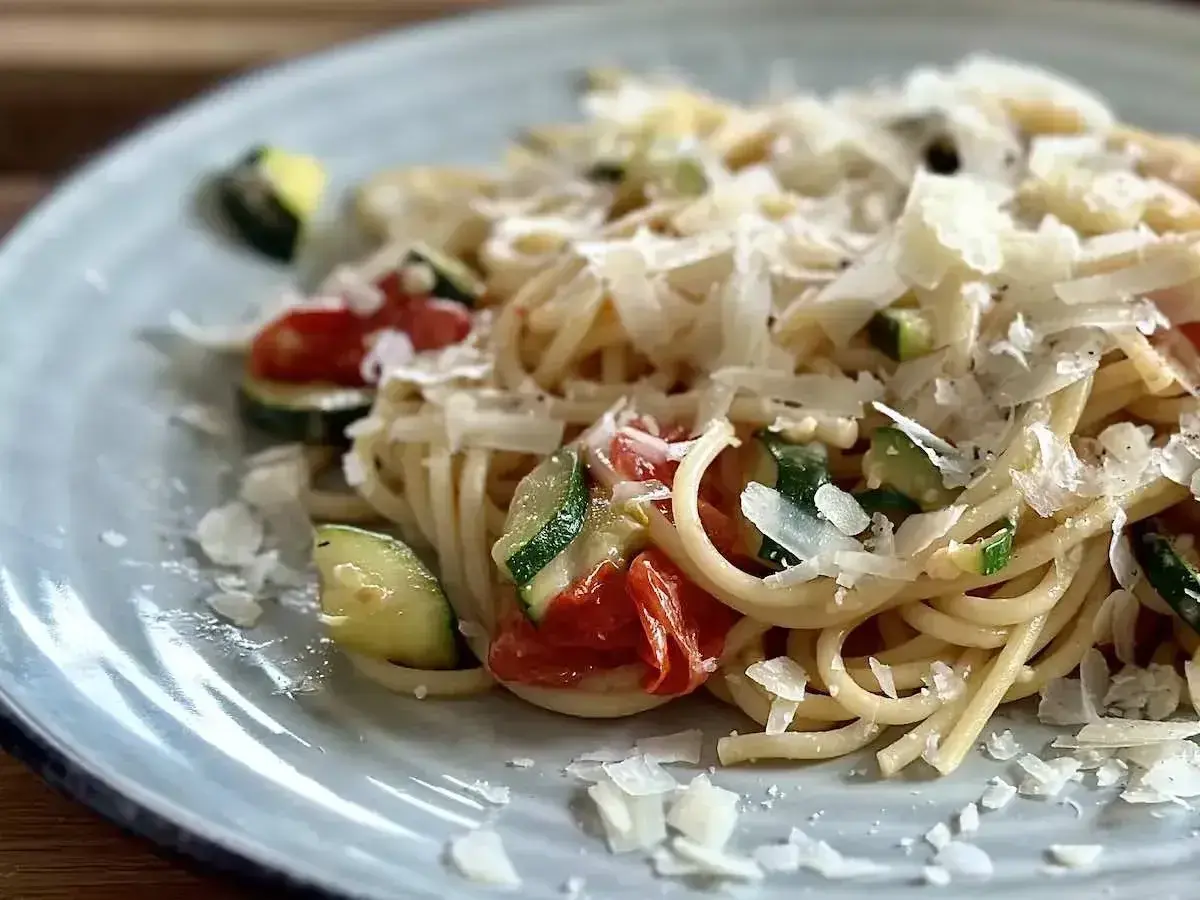 Pyszny makaron z pomidorkami koktajlowymi i cukinią, posypany parmezanem. Idealny letni posiłek.