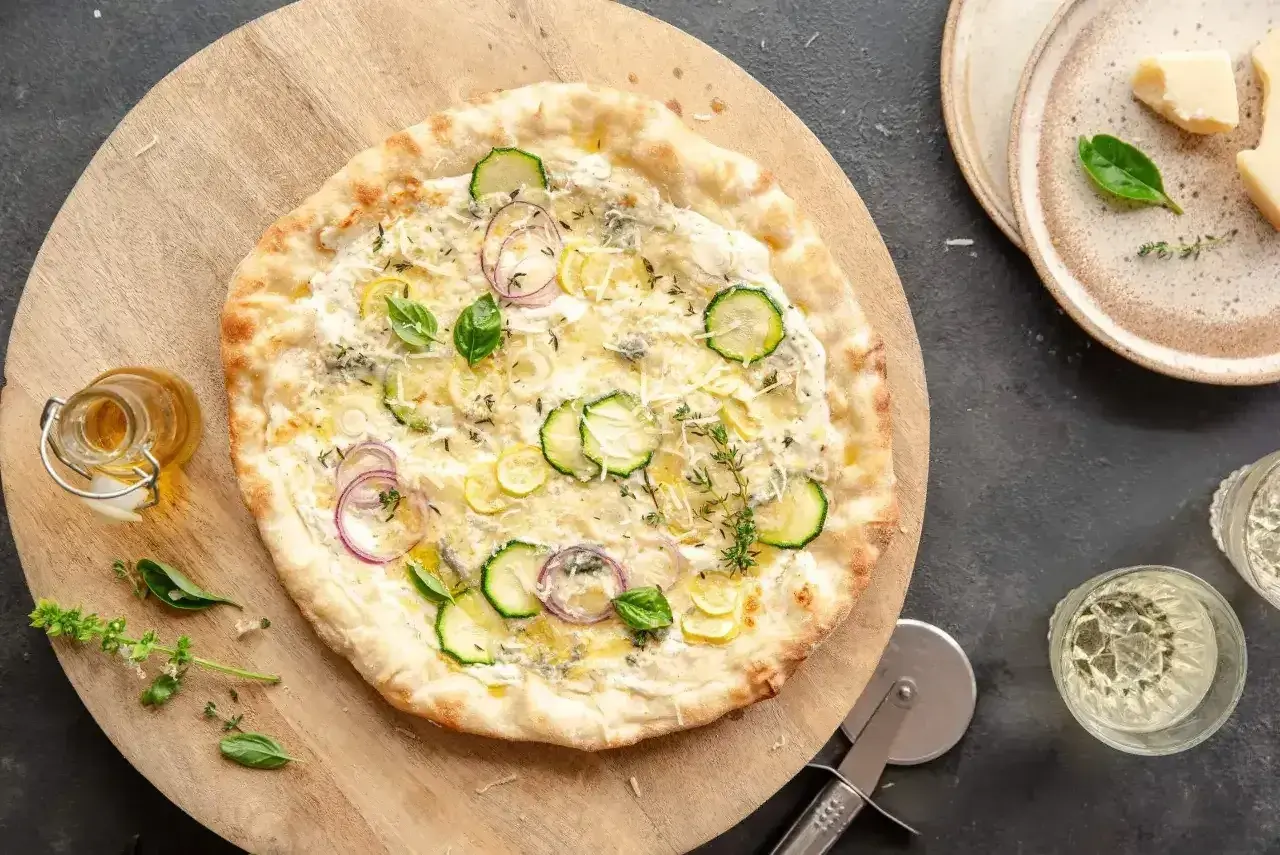 Pyszny spód do pizzy z cukinią, cebulą i ziołami, podany na drewnianej desce.