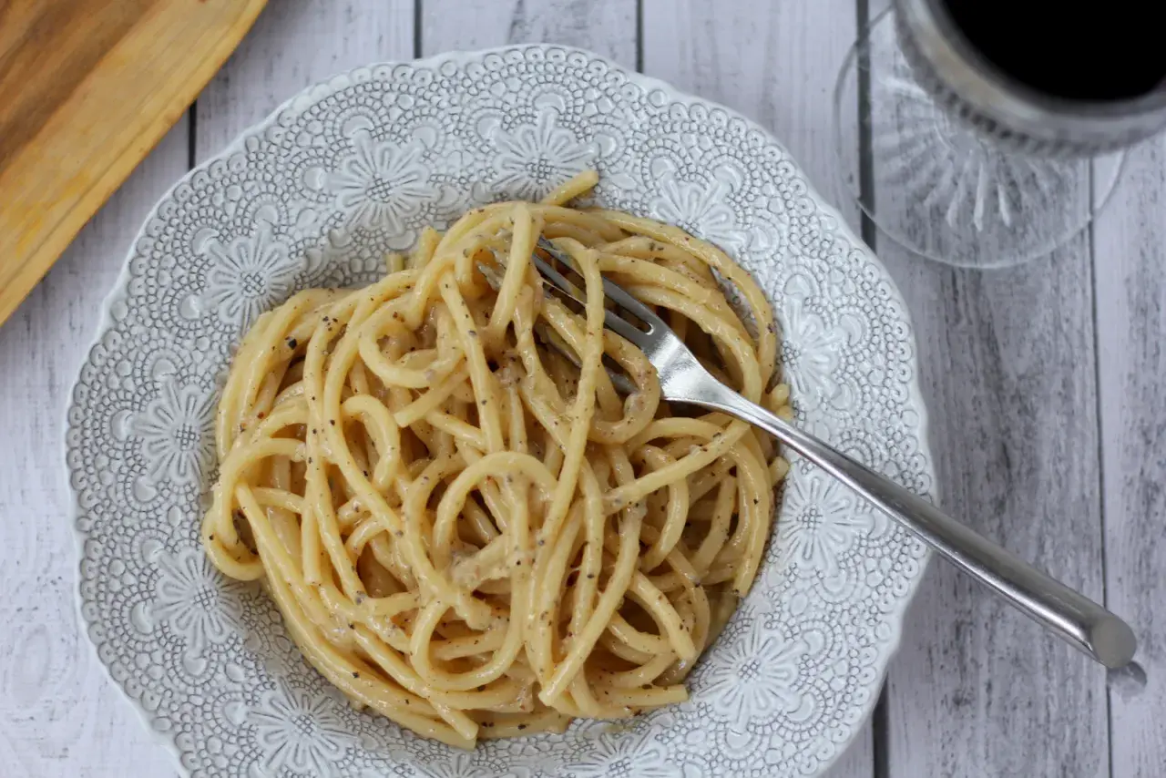 Porcja pysznego cacio e pepe na ozdobnym talerzu, z widelcem w makaronie.