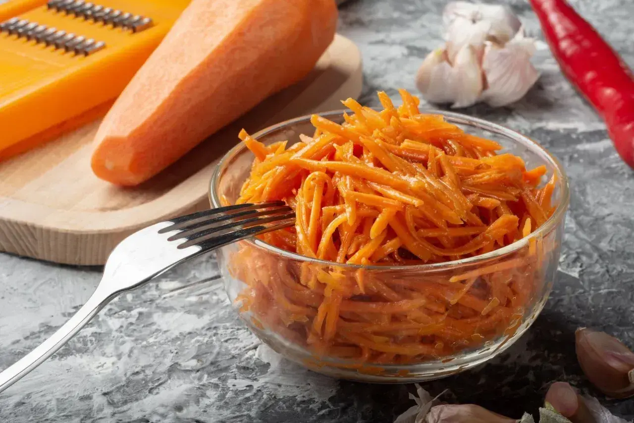 Pyszna surówka z marchewki, gotowa do podania. Obok świeża marchewka, tarka, czosnek i papryczka chili.