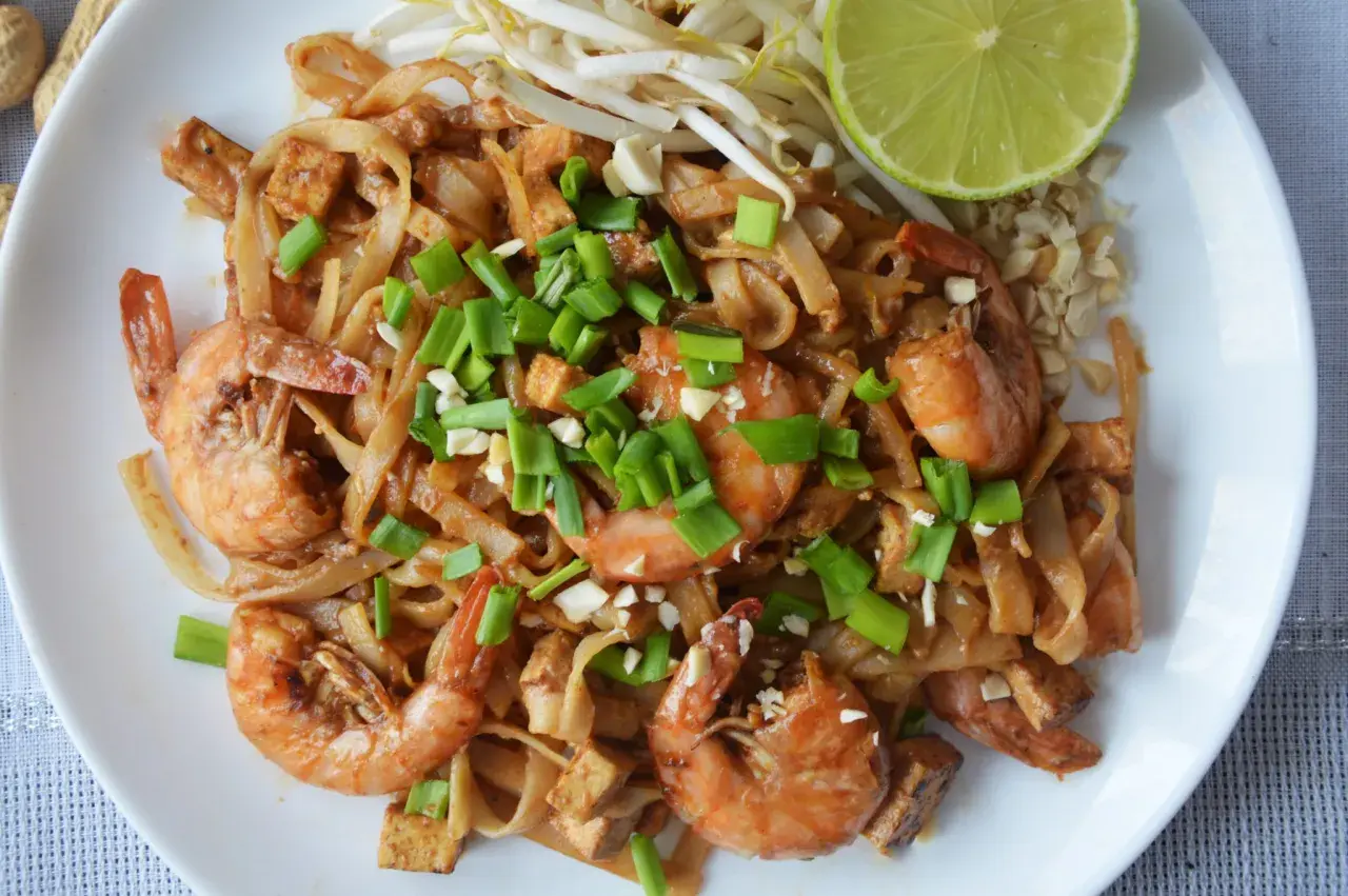 Pyszne pad thai z krewetkami, makaronem ryżowym, tofu i szczypiorkiem, podane z limonką i orzeszkami ziemnymi.