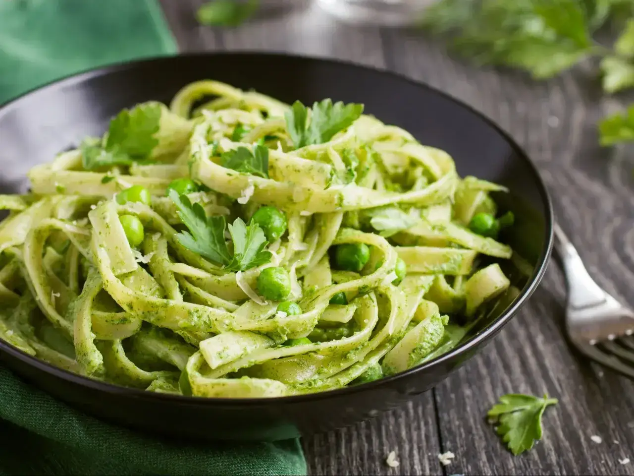 Talerz pełen tagliatelle z zielonym pesto, groszkiem i listkami pietruszki. Pyszny makaron z pesto kusi świeżością.