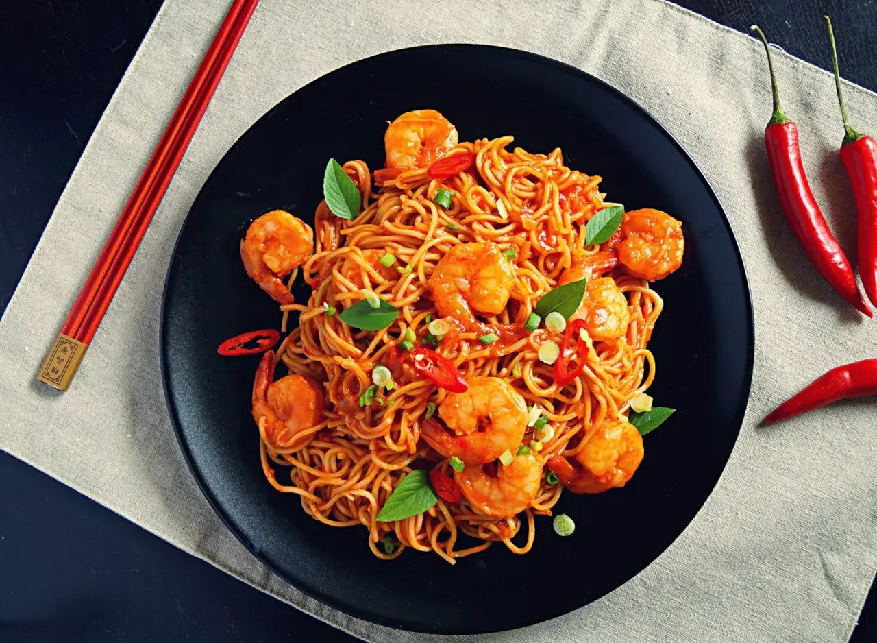 Pyszny pad thai z krewetkami, udekorowany bazylią i papryczkami chili. Idealny na szybki obiad.