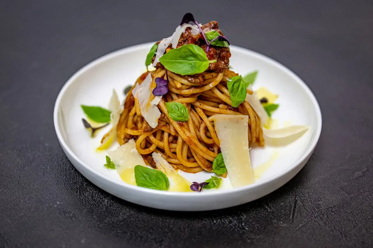 Pyszne spaghetti alla norma z sosem pomidorowym, bakłażanem i parmezanem, ozdobione listkami bazylii.