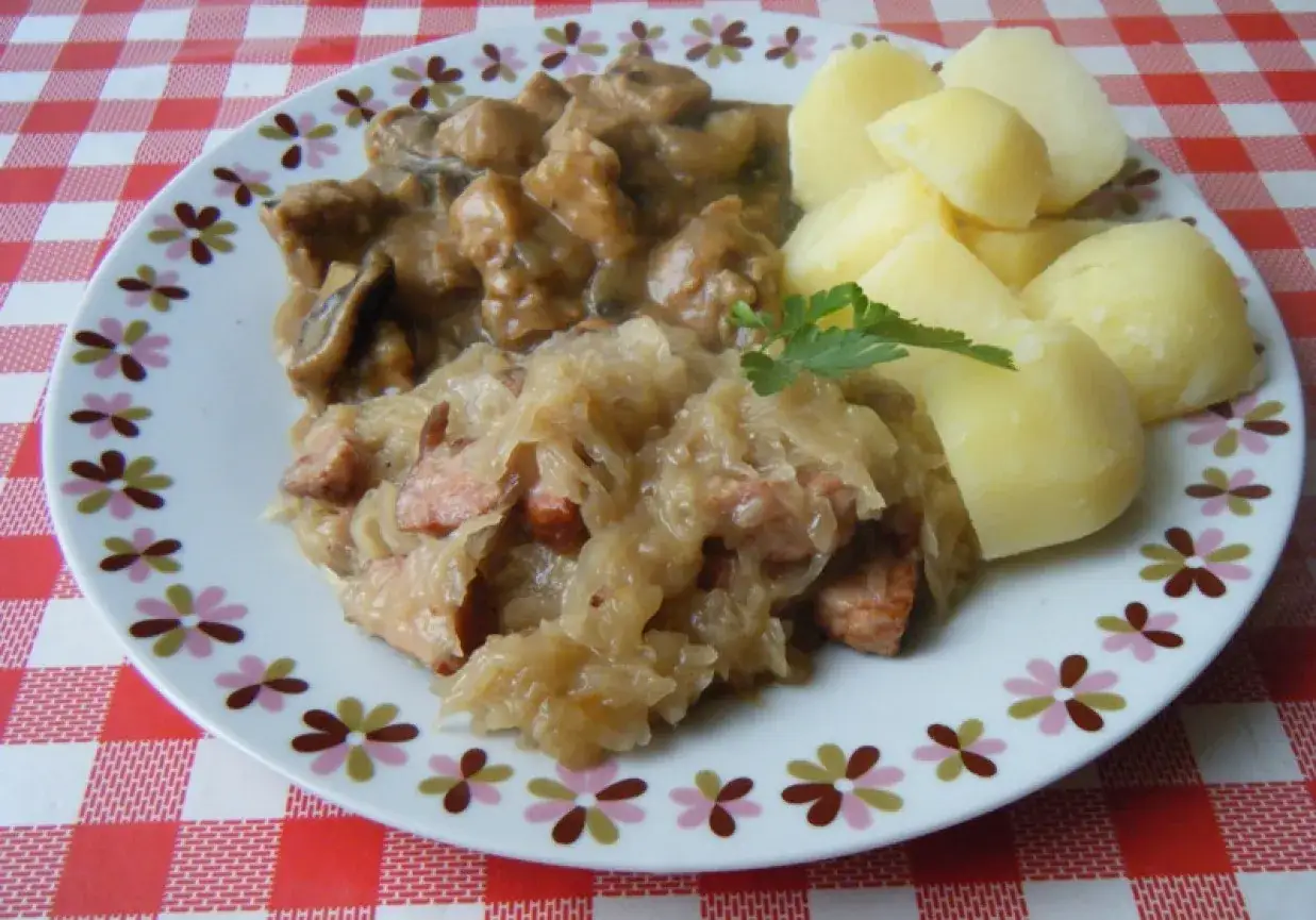 Porcja sycącej kapusty kiszonej gotowanej z kiełbasą, podana z ziemniakami i gulaszem grzybowym.