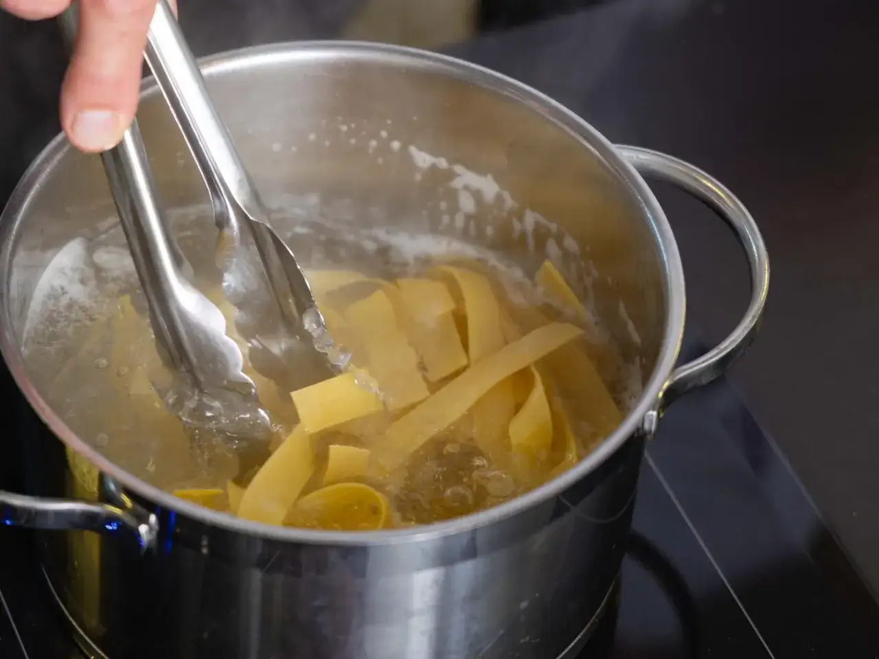 Szczypce wkładają szeroki makaron do wrzącej wody. Oto jak ugotować makaron, by był idealny.