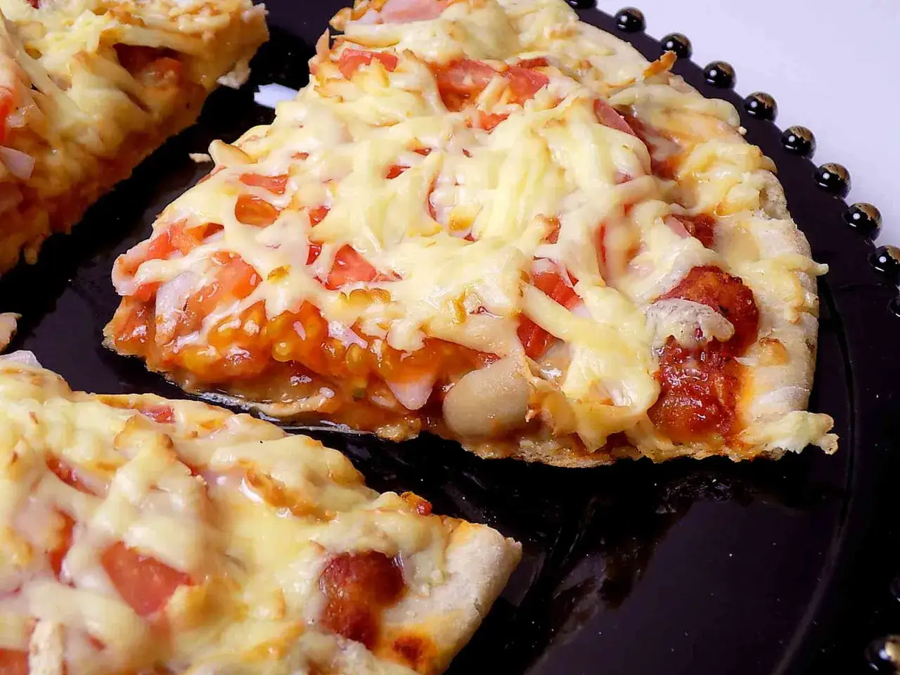 Pyszna pizza z patelni, z ciągnącym się serem, pomidorami i kawałkami kiełbasy, podana na czarnym talerzu.