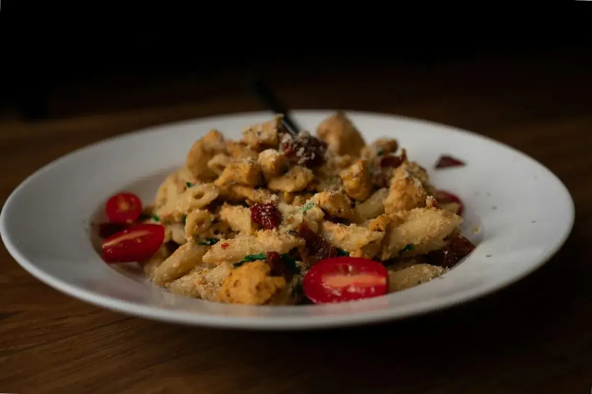 Penne z kurczakiem i aromatycznymi suszonymi pomidorami, posypane parmezanem.