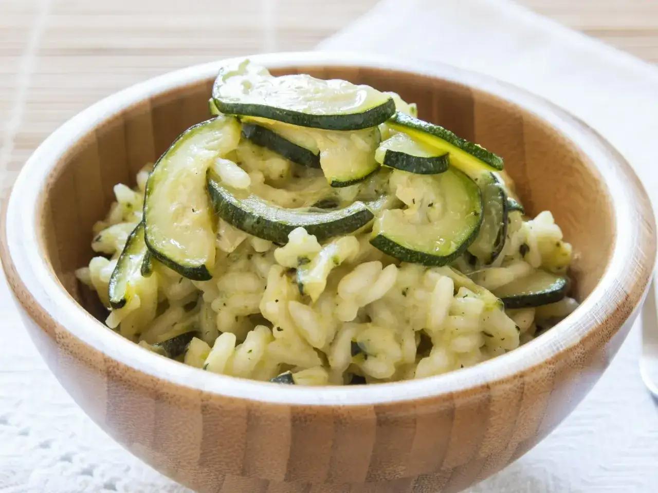 Pyszne risotto z warzywami, z cukinią w roli gł&oacute;wnej, podane w drewnianej misce.
