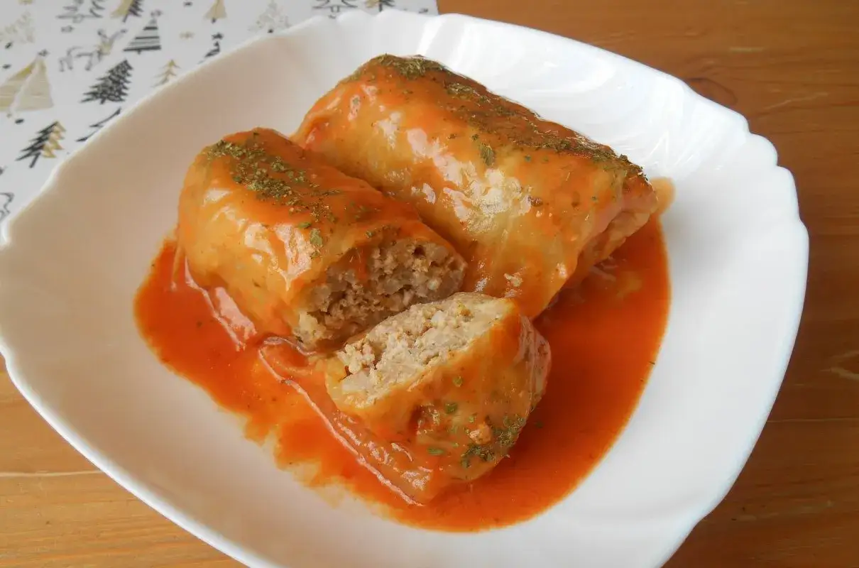 Pyszne gołąbki bez zawijania, polane sosem pomidorowym, posypane ziołami. Jedna sztuka przekrojona, ukazująca farsz z ryżu i mięsa.
