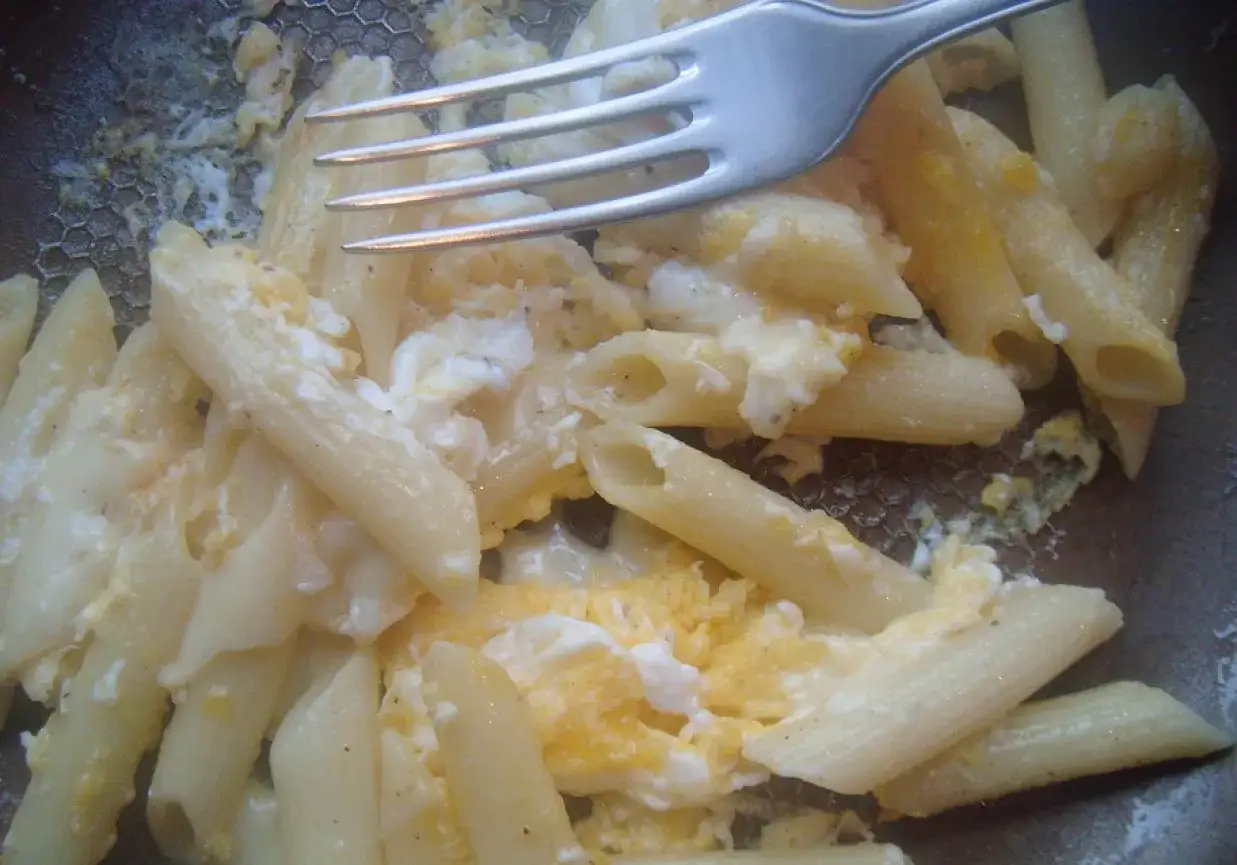 Penne z jajkiem, proste i sycące danie. Widok z góry na talerz z makaronem i jajecznicą, obok leży widelec.