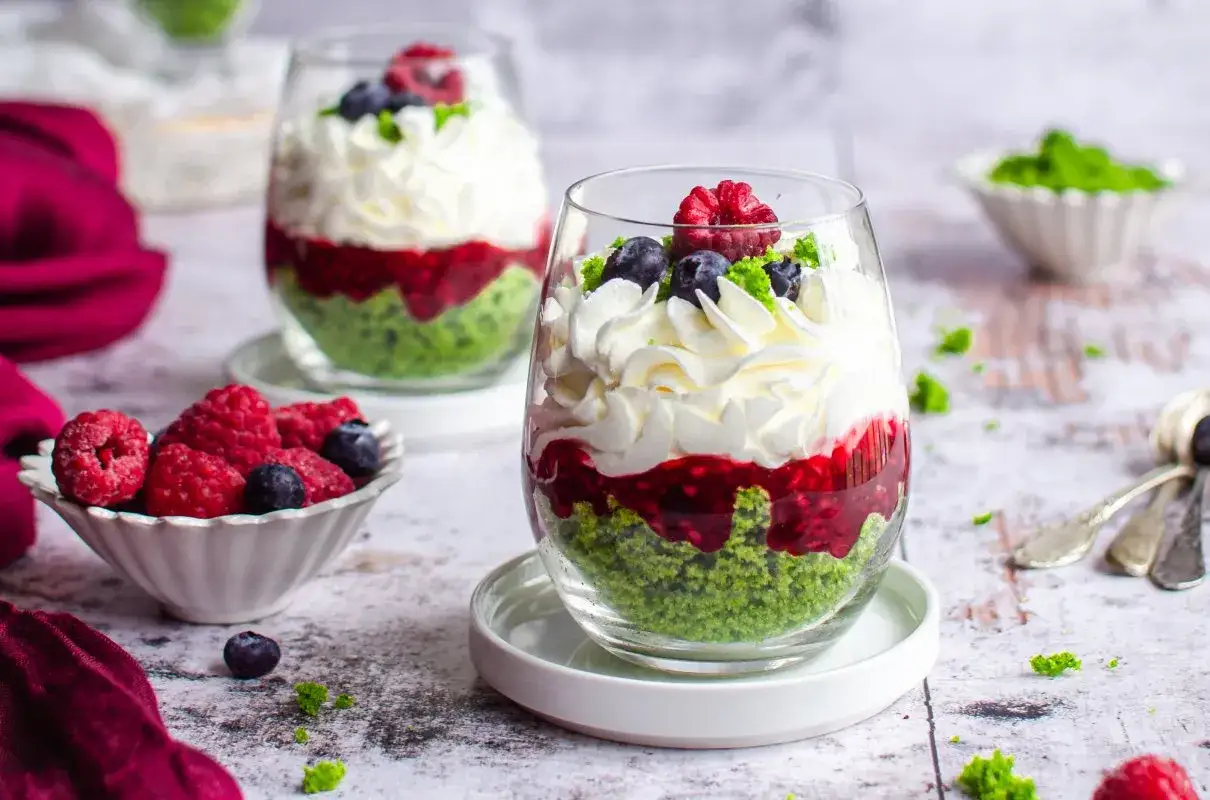 Pyszne ciasto leśny mech z mascarpone w pucharkach, przełożone malinową frużeliną i udekorowane owocami.