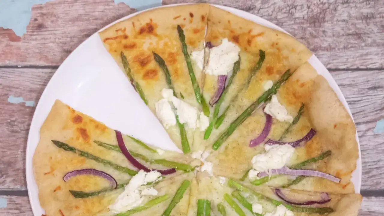 Pizza ze szparagami i serem feta na białym talerzu, na drewnianym tle.