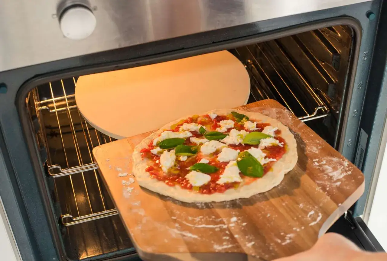 Ręka wsuwa pizzę z mozzarellą i bazylią do rozgrzanego piekarnika. Już niedługo będzie gotowa do jedzenia!