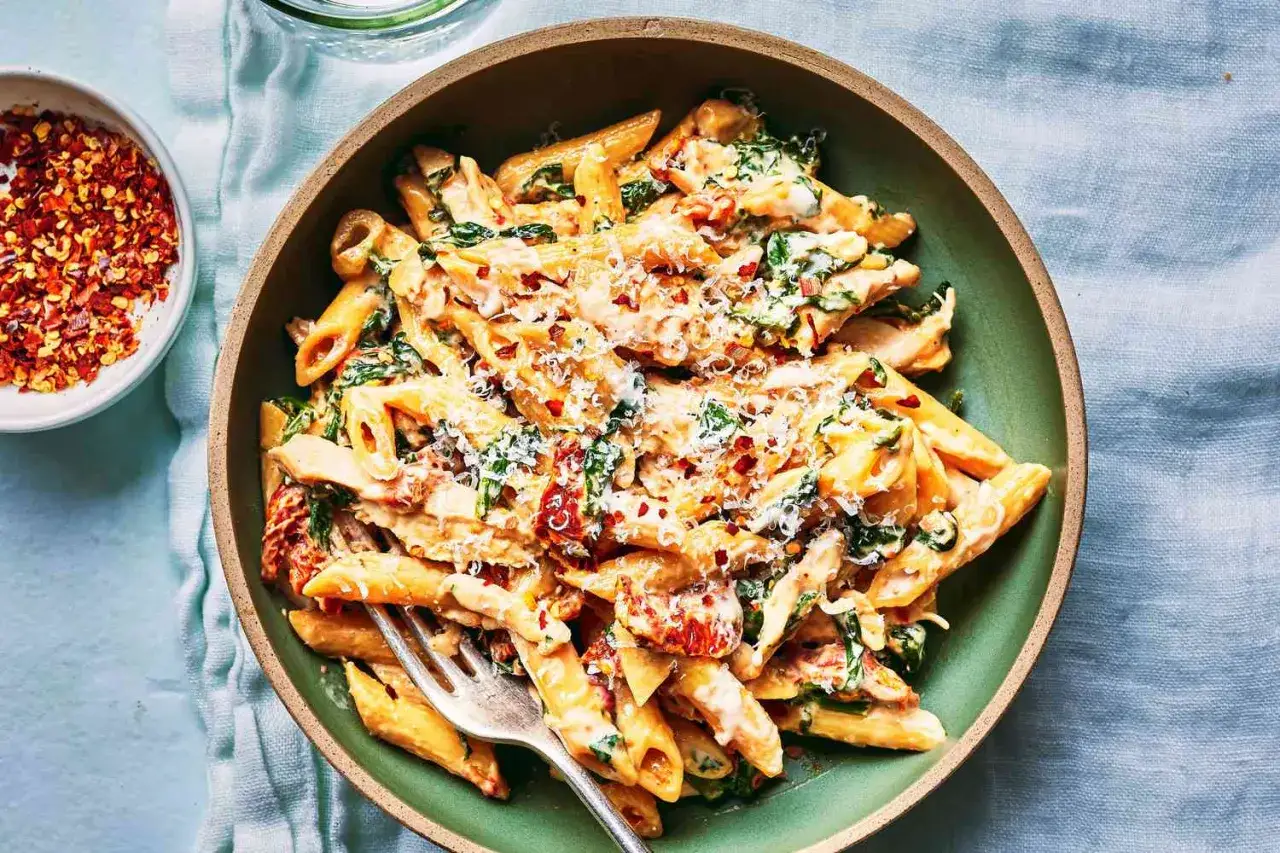 Penne w kremowym sosie ze szpinakiem i suszonymi pomidorami, posypane parmezanem i płatkami chili.