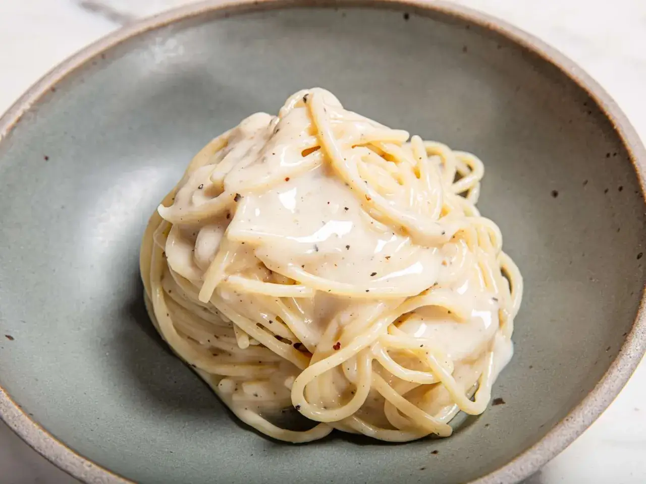 Porcja kremowego cacio e pepe w szarej misce, z widocznymi ziarnami pieprzu.
