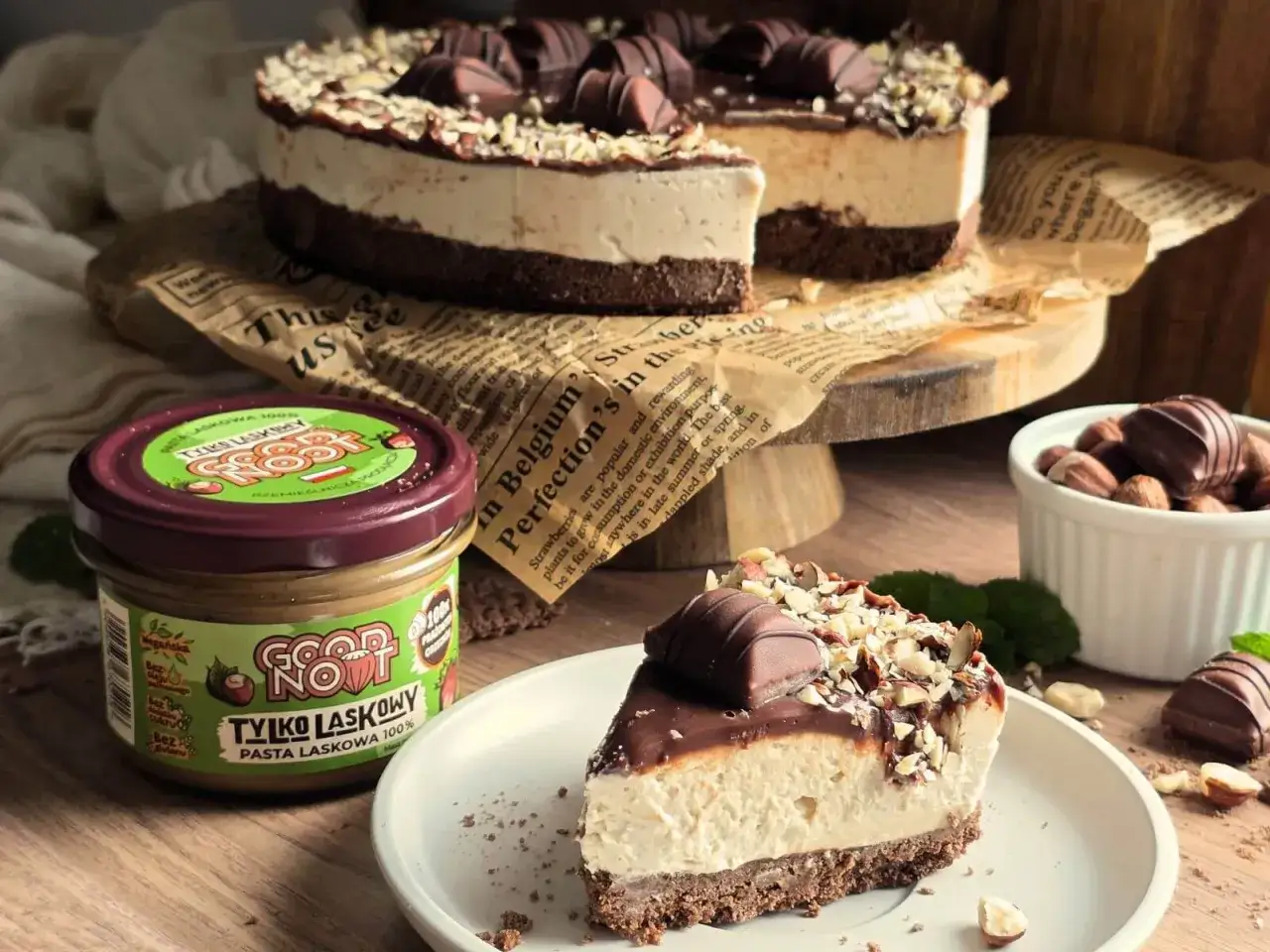 Ciasto Kinder Bueno z mascarpone, udekorowane orzechami i czekoladkami. Obok słoik pasty z orzech&oacute;w laskowych.