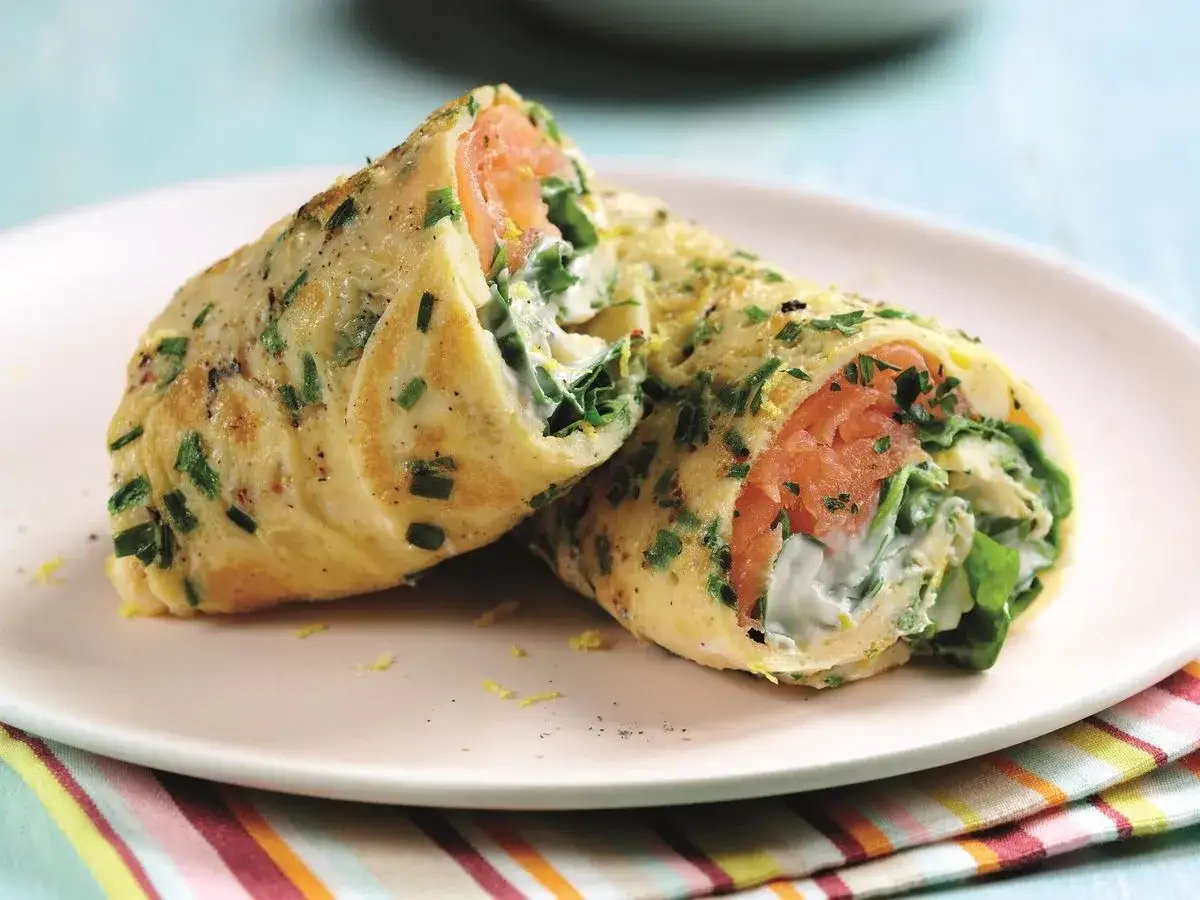 Roladki z omletu z łososiem, szpinakiem i kremowym serkiem, posypane szczypiorkiem. Pyszna tortilla z łososiem na śniadanie.