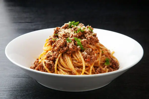 Pyszne spaghetti z bogatym sosem bolognese, posypane parmezanem i natką pietruszki. Idealne danie z makaronem z mięsem mielonym.